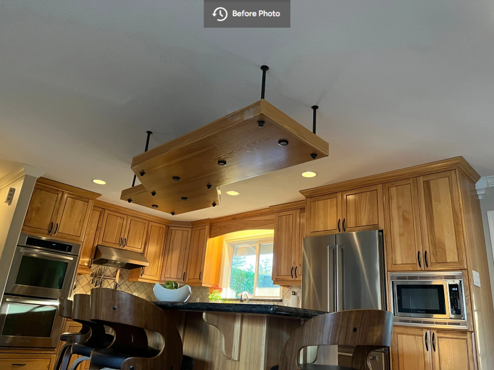 Outdated kitchen with wood cabinetry, stainless steel appliances, and a ceiling-mounted structure over the central island before renovation.