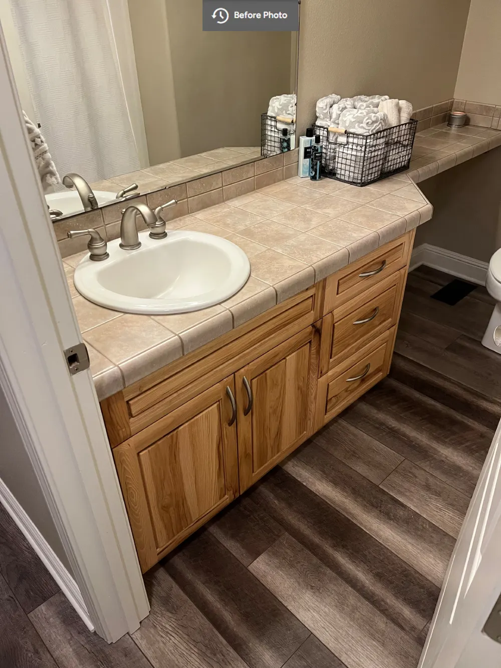 Traditional bathroom vanity featuring oak cabinetry, tiled countertop, integrated white sink, and large mirror before its remodel.
