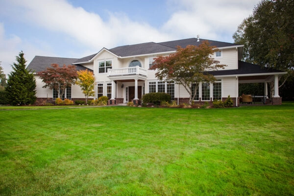 Wide-angle view of a luxury multi-story home featuring structural additions, a covered entry porch, balcony, and manicured front lawn.