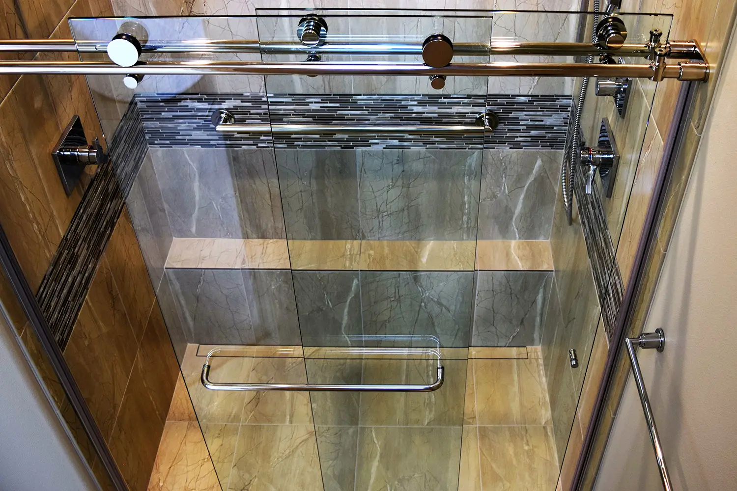 Luxury walk-in shower with marble-look tile, a linear mosaic accent, polished chrome fixtures, and a frameless sliding glass door.