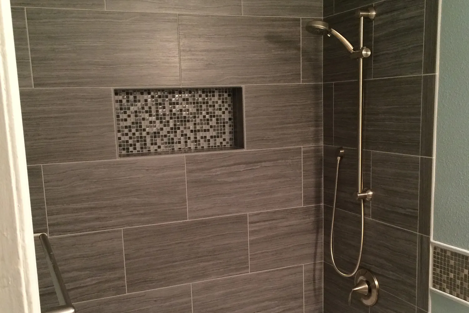 Modern shower with large-format gray wood-look tile, a recessed glass mosaic niche, and a brushed nickel handheld showerhead.