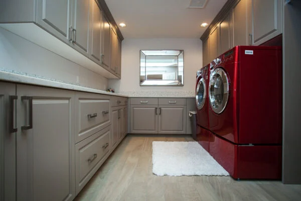 Custom laundry room with gray cabinetry, quartz countertops, and vibrant red front-load appliances designed and built by Black Cat Design Build LLC.