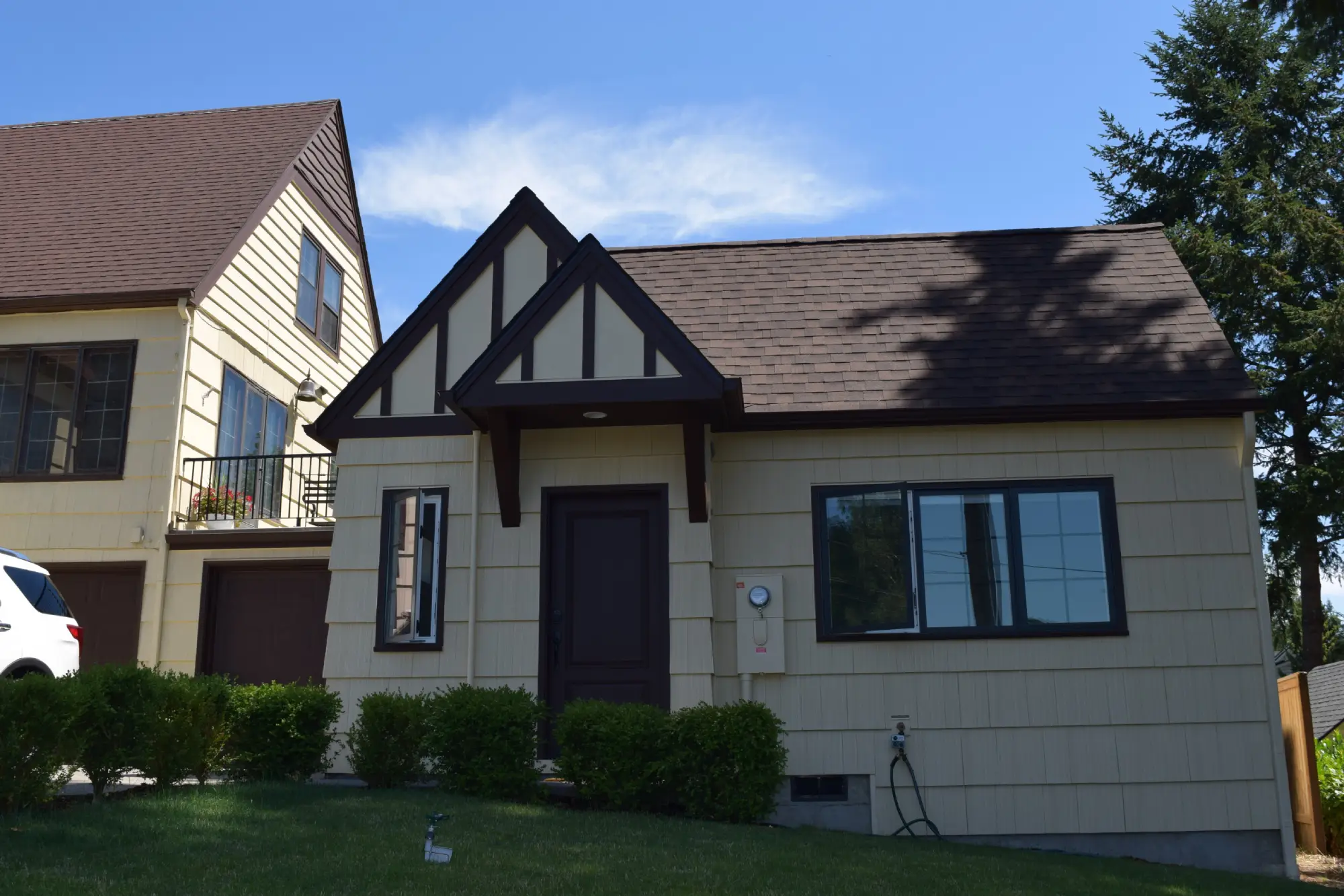 Small residential ADU with light shingle siding and dark architectural details standing beside the main home.