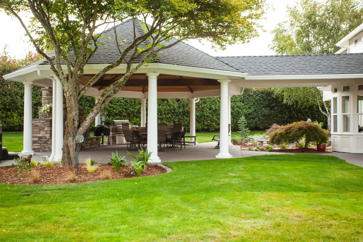 A modern outdoor living space with pavilion structure, dining set, and built-in cooking area.