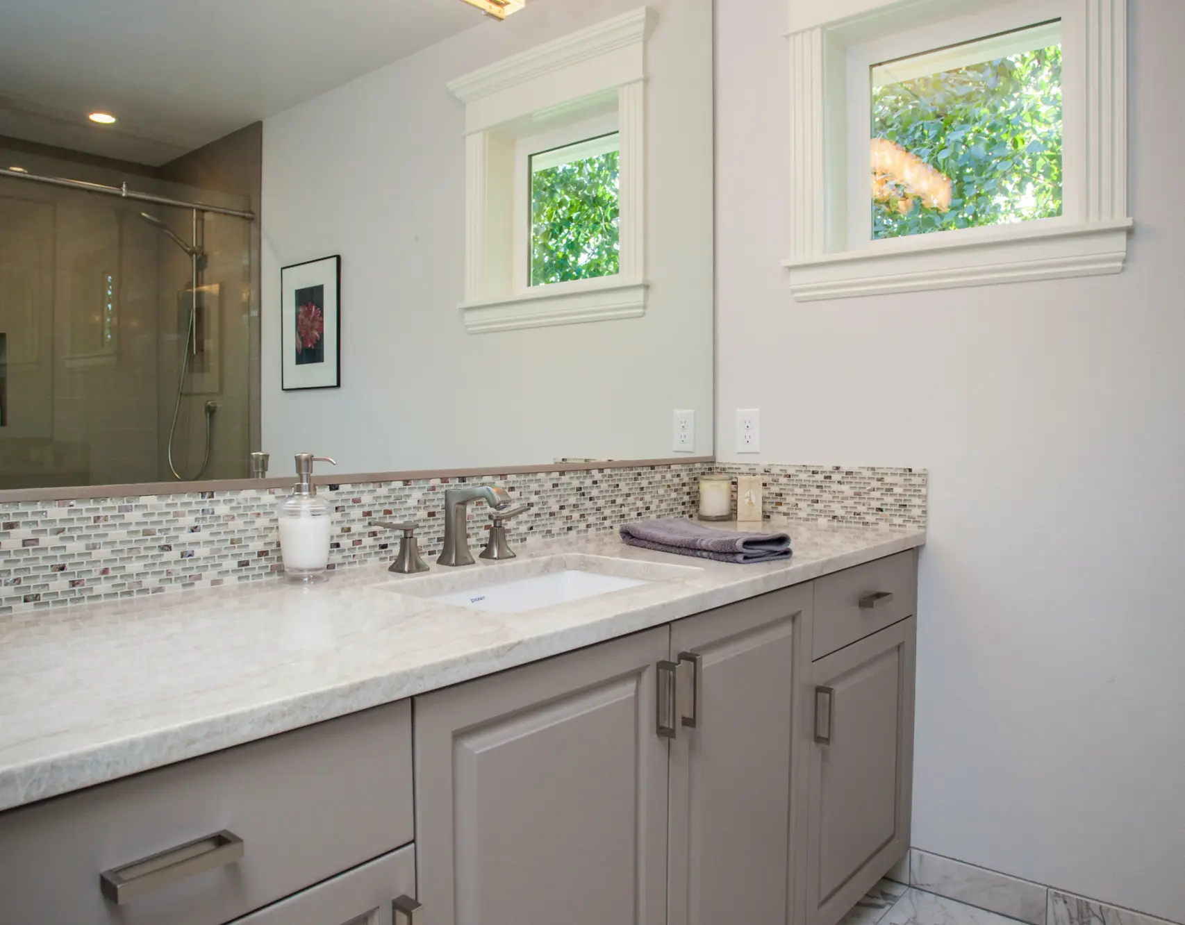 Elegant vanity featuring soft gray cabinetry, an undermount sink, and a glass tile backsplash, built by Black Cat Design Build LLC.