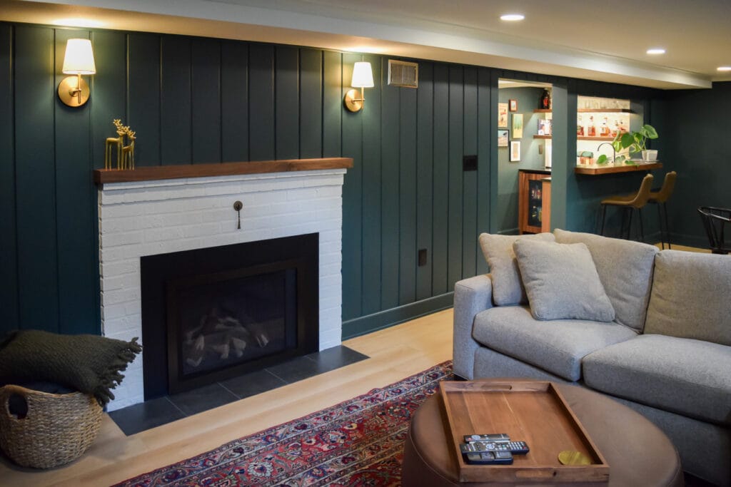 Custom basement remodel in Vancouver, WA featuring a retrofitted gas fireplace insert, light luxury vinyl plank flooring, and dark green wainscoting.