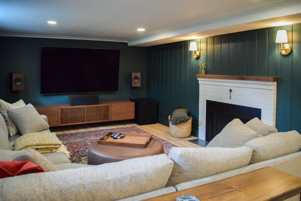 Moody basement entertainment lounge with a sectional sofa, media console, and multi-zone recessed lighting.