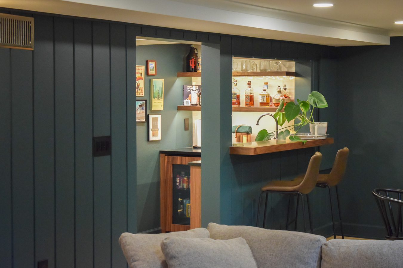 View from the living area into a custom basement bar, showing painted drywall soffits cleanly concealing the mechanical ductwork.