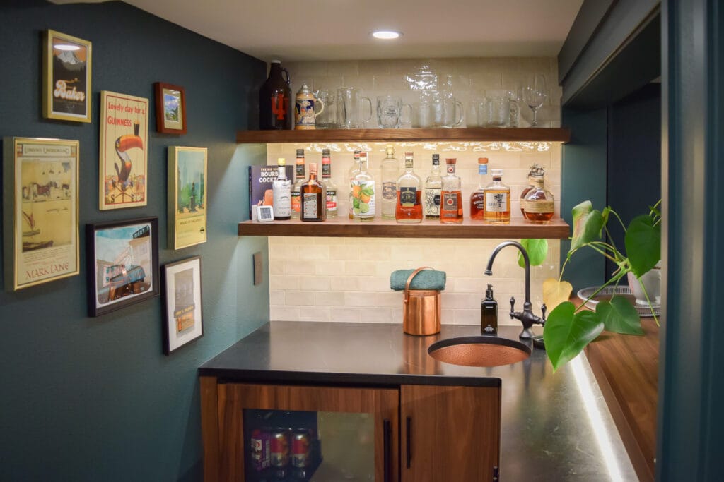 Close-up of a custom basement bar with soapstone countertops, an integrated walnut beverage cooler panel, and under-shelf LED lighting.